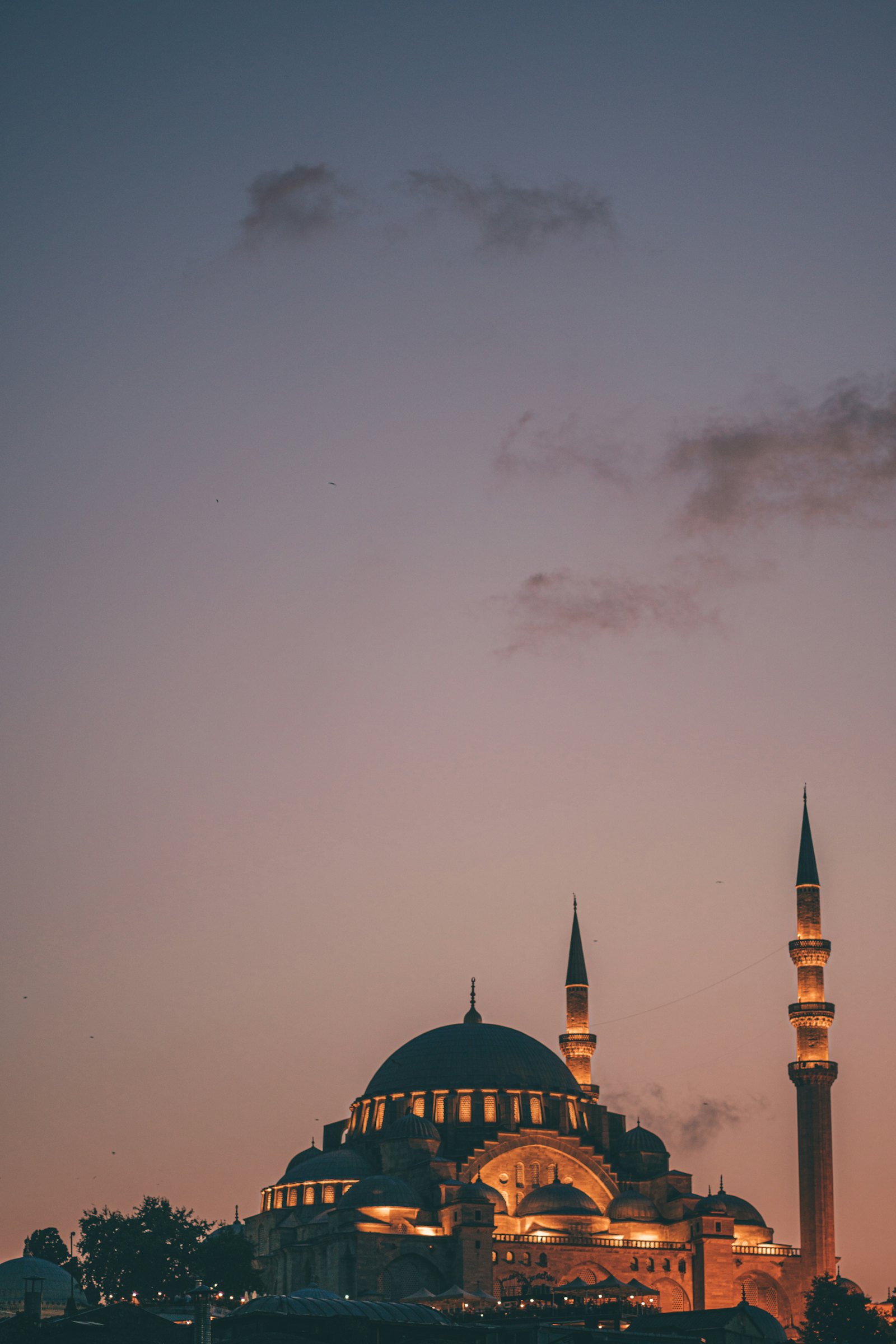 A domed mosque and two minarets lit in warm light under an evening sky